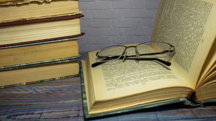 Pile of old books with reading glasses on desk