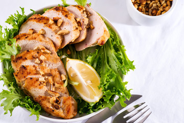 Grilled chicken breast with fresh frize salad, peanuts and lemon on a plate on stone background