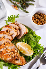 Grilled chicken breast with fresh frize salad, peanuts and lemon on a plate on stone background