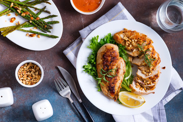 Grilled chicken breast with grilled asparagus and lemon slice on dark stone background . Paleo diet.