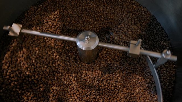 Beautiful cinematic shot of industrial coffee roasting process. Fresh and aromatic beans are mixed in cooling drum roaster for small batch and locally produced organic beans