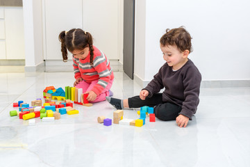 Zero waste. Two young children playing together with plastic free wooden toys building blocks. Kids picking up,examining and stacking blocks while sitting on the floor indoors at home or kindergarten.