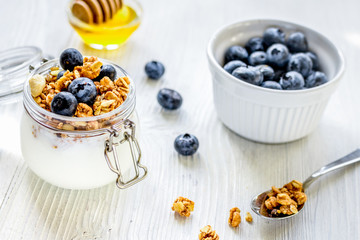 Homemade granola with blueberries in jar on white kitchen background