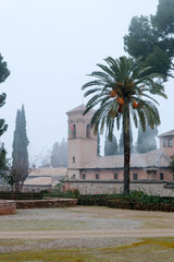 Fototapeta na wymiar old medieval church inside the Alhambra walls, Granada, Spain surrounded by palms and cypress in morning haze