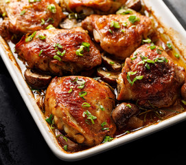 Roasted chicken thighs with mushrooms, garlic and herbs in a baking dish, close-up
