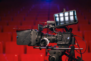 Fototapeta na wymiar Professional video camera in a movie theater with red seats and blue light projector
