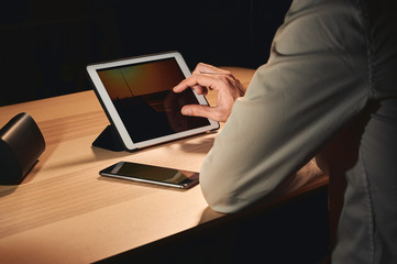 side view of a man using his tablet computer to see a picture of a sunset. There is a hand zooming in on the picture