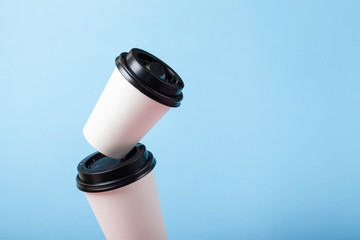 tower of different size white paper coffee cups with black lid on pastel blue and pink background