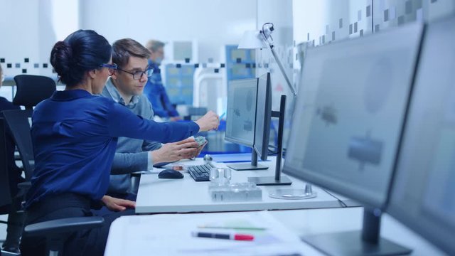 Modern Factory: Male Industrial Engineer Explains to Female Project Supervisor Functions of the Machine Part Comparing it to one on Computer Screen. They use CAD Software for Design, Development