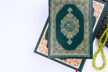 Holy Quran with arabic calligraphy meaning of Al Quran and tasbih or rosary beads over white background, copy space.