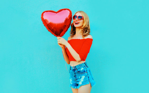 Portrait happy smiling woman holding red heart shaped air balloon on colorful blue background