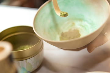 woman holding  Matcha green powder tea in clay bowl with a traditional bamboo spoon and a tea can