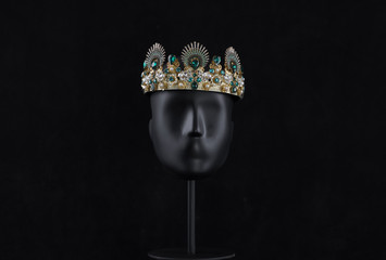 black mannequin head with crown isolated on black background