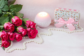 a bouquet of pink roses, a gift in a box, a candle and pearl beads