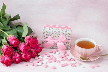 a bouquet of pink roses, a gift in a box, heart-shaped candies and tea in a cup