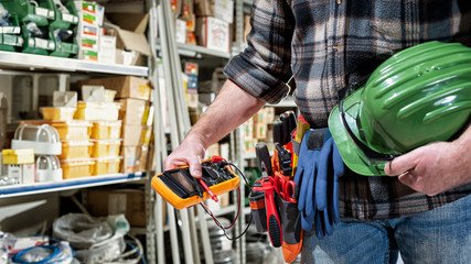 Electrician holds multimeter tester in hand, helmet with protective goggles. Construction industry, electrical system.