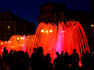 Red neon lights illuminate the jets of a powerful urban singing fountain in the late evening.