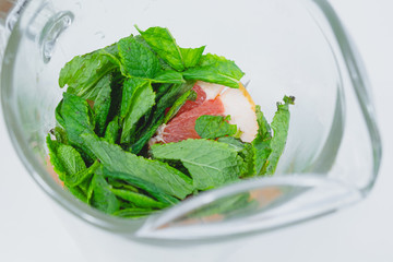 Fresh peppermint leaves and grapefruit slices in a glass, close-up view. Preparing tonic water or...
