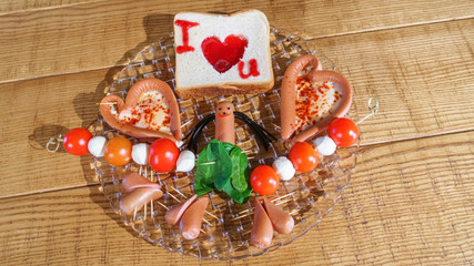 Breakfast on Valentine's Day. Fried eggs, sausage and bread in the shape of a heart and fresh vegetables on wooden background.. Top view. Valentines day concept