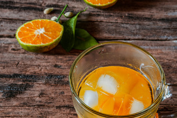 A glass of orange juice on a vintage wooden table, complemented by slices of fresh local oranges and their leaves. In Indonesia this drink is called jus jeruk.
