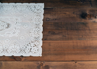 White lace napkin on brown wooden background. Vintage background with white crochet lace.