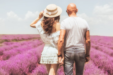 Back view lovely young couple at the lavender field, holding hands. Photo of beautiful young couple man and woman laughing and walking outdoor in lavender field