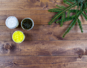 Cosmetic flatlay with banks of srubs, coffee, grassy, lemon, nut scrubs and spruce leave on a brown wooden background.