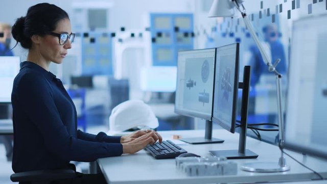 Beautiful Female Engineer Working on Personal Computer in the High-Tech Industrial Factory, She Uses CAD Software to Model Heavy Industry High Tech Mechanism 3D Model. Side View Portrait 