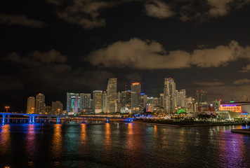 Miami city skyline panorama at dusk with urban skyscrapers and bridge over sea with reflection.