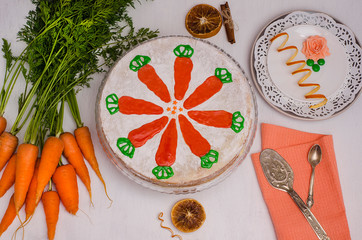 Carrot Cake Day. Carrot cake on a white wooden background with a served saucer and carrots, decorated with icing in the form of carrots. View from above. Homemade holiday pastries