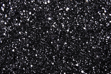 Real falling snow on a black background for use as a texture layer in a photo design. Flying snowflakes illuminated by a lantern on the background of the night sky