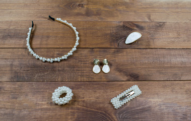 Flatlay set jewelry pearls accessories on wooden brown background. Hair band, ring, earrings, scrunchy and hairpin for hair.