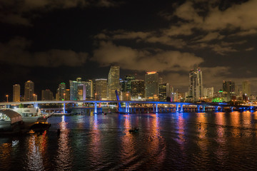 Miami city skyline panorama at dusk with urban skyscrapers and bridge over sea with reflection..