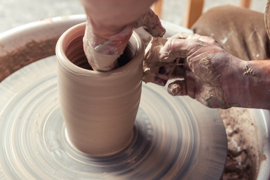 Side view of potter's hand making a vase of white clay on throwing-wheel in ceramics studio, concept of creativity and art, horizontal photo, selective focus