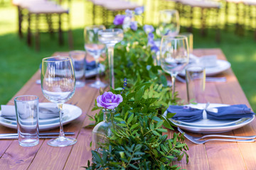 Beautifully decorated wooden table in a summer open-air cafe. Green branch and fresh flowers table decoration
