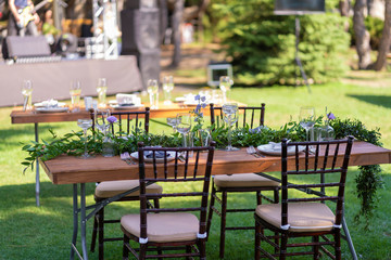 Beautifully decorated wooden table in a summer open-air cafe. Green branch and fresh flowers table decoration
