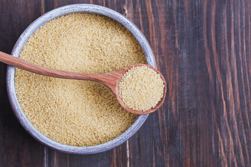 Dry couscous in a bowl and spoon on wooden background,