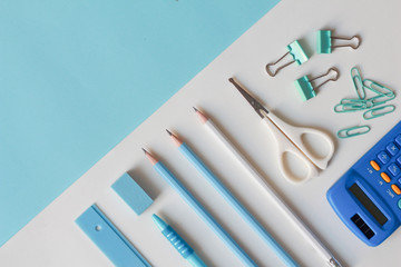 Stationary school supplies in white and blue tone, Scissors, pencils, paper clips,calculator, notepad  on blue and white background, Flat lay.