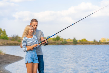 Happy young couple fishing by lakeside a
