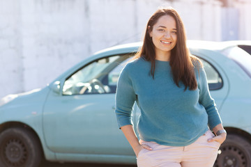 Happy plus size woman posing outside of the blue rental car in sunny day