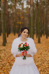 Beautiful happy bride with a wedding bouquet in the forest in autumn.