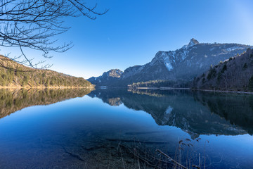 Stunning view of the Alpsee lake in winter with the Neuschwanstein and Bavaria Alps in background