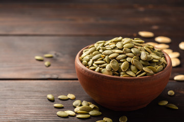 Pumpkin seeds in ceramic bowl on dark wooden background. Selective focus.