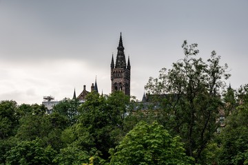 Fototapeta premium The ancient tower of the Gilbert Scott Building of University of Glasgow behind the green Kelvingrove Park in Scotland