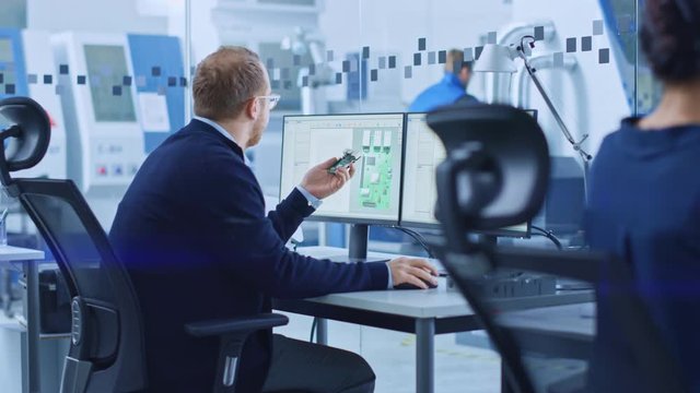 Electronics Factory: Male Electrical Engineer Holds PCB Prototype, Works on Computer, uses CAD Software to Develop Microchips, Semiconductor and Telecommunications Equipment. Manufacturing Facility