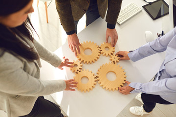 A group of business people holds wooden wheels with teeth in their hands on an office white table.