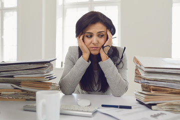 Woman brunette businesswoman in glasses with a mountain of documents on the table tired depressed...