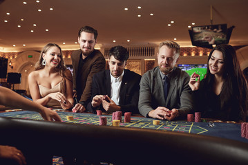 A group of young smiling people are playing roulette in a casino.
