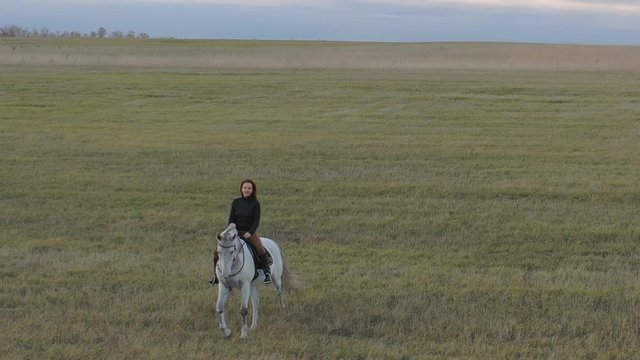 A red-haired woman rides a white horse.