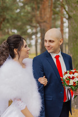 Happy bride and groom are standing in the autumn forest holding hands.